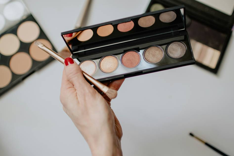 Two diverse makeup artists reviewing portfolios in a well-lit studio with competition trophies on display